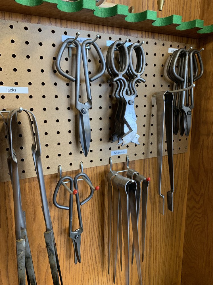 Set of metal tools including scissors and tongs on a pegboard wall.