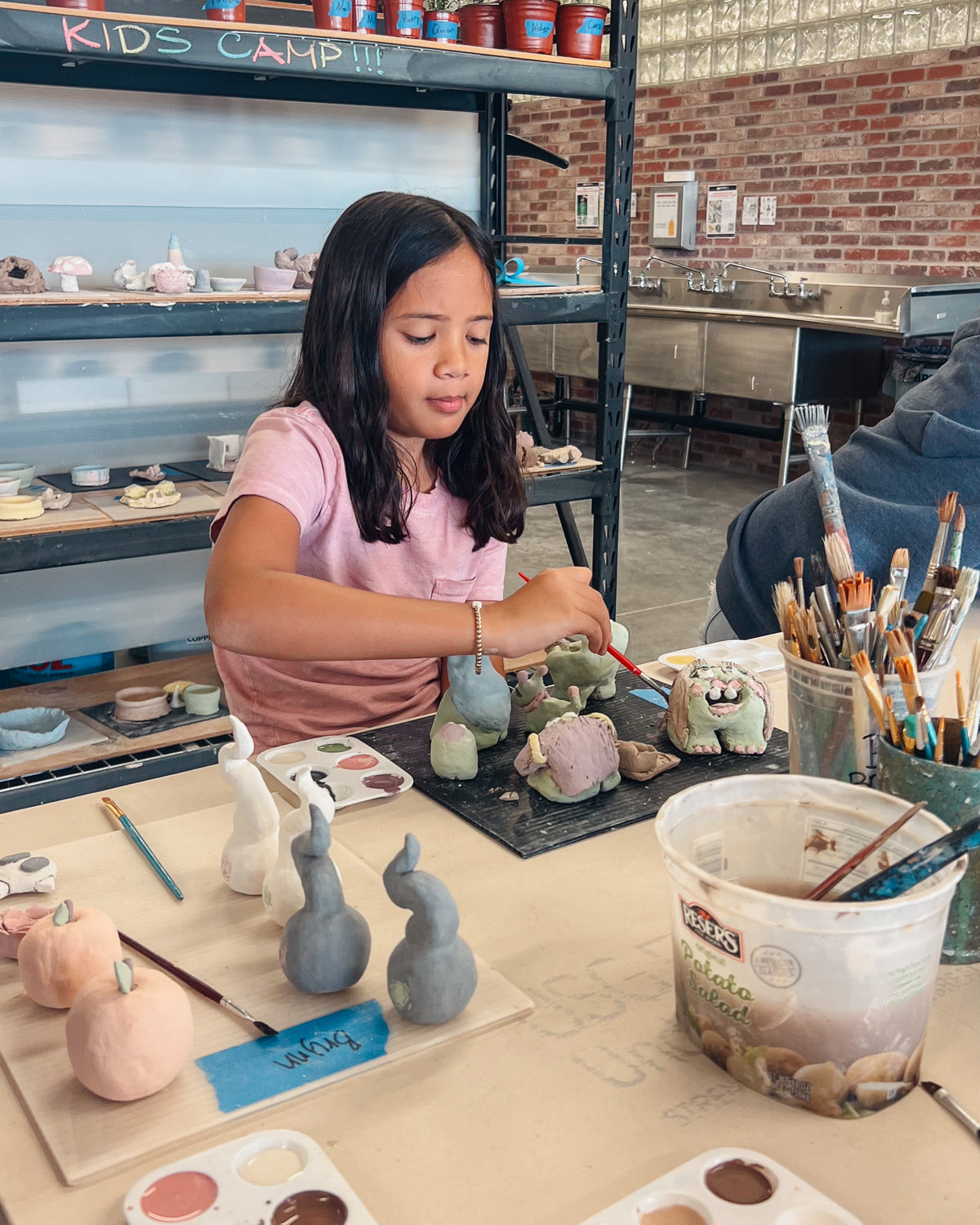 Child painting ceramic figurines at a kids camp in an art studio.